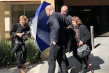 Dragi Stojanovski uses an umbrella to shield his brother and mother from a photographer as they leave the Coroners Court.