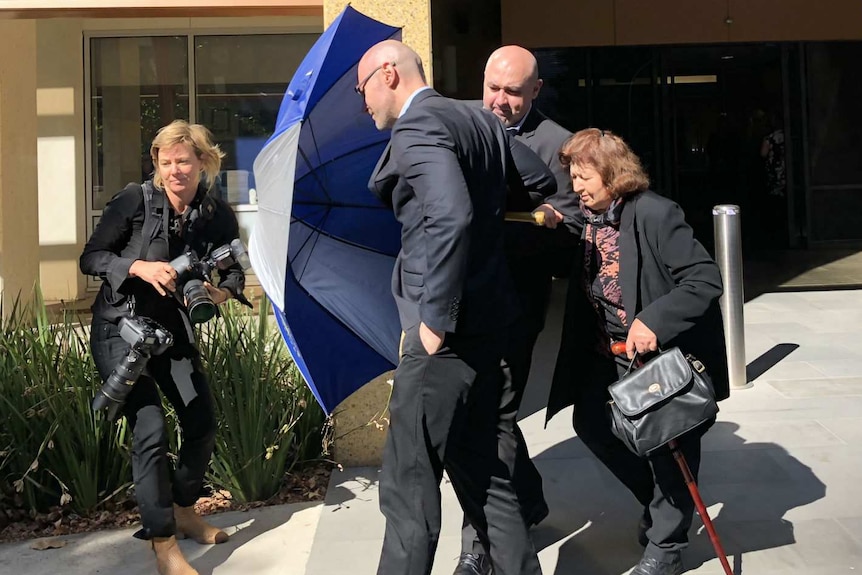 Dragi Stojanovski uses an umbrella to shield his brother and mother as they leave the Coroners Court at an earlier hearing