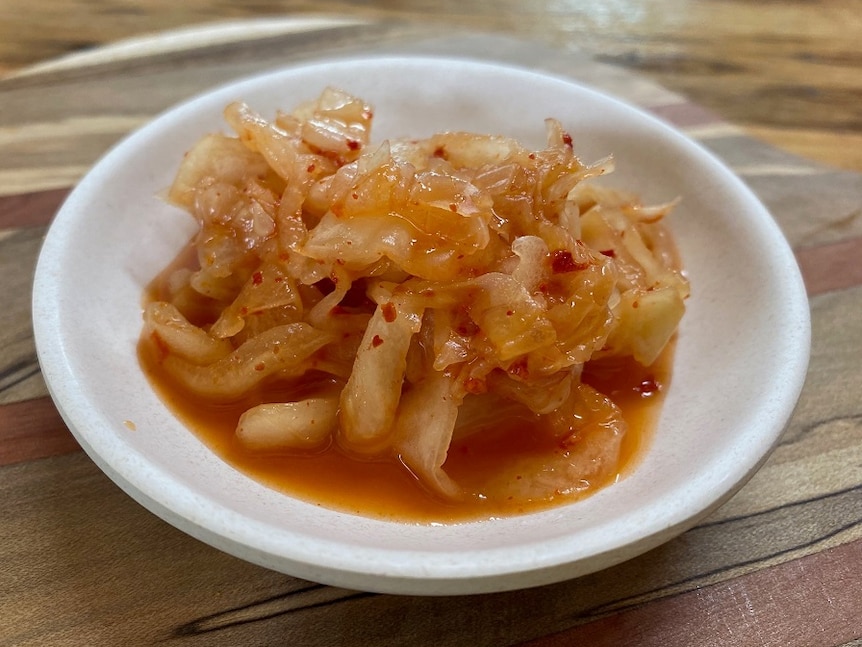 A white plate filled with red kimchi on a wooden table.