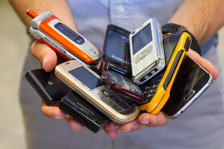 Close-up of man's hands holding a pile of mobile phones.