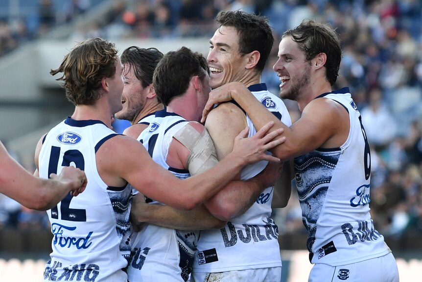 Jeremy Cameron smiles while Cats players surround him and hug him