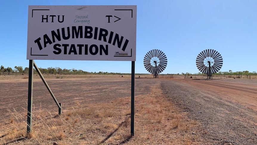 A wide shot of a sign reading Tanumbirini Station with windmills in the distance.