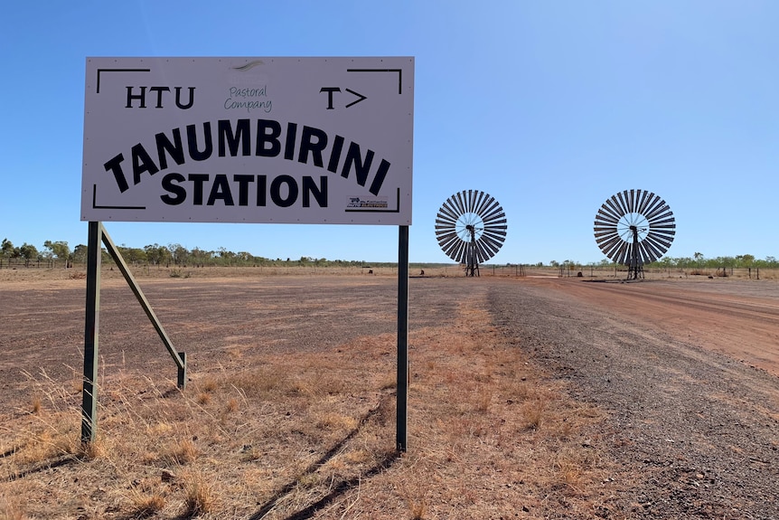 A wide shot of a sign reading Tanumbirini Station with windmills in the distance.