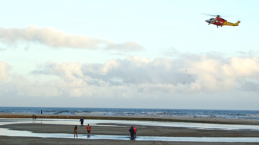 A helicopter hovers above a beach