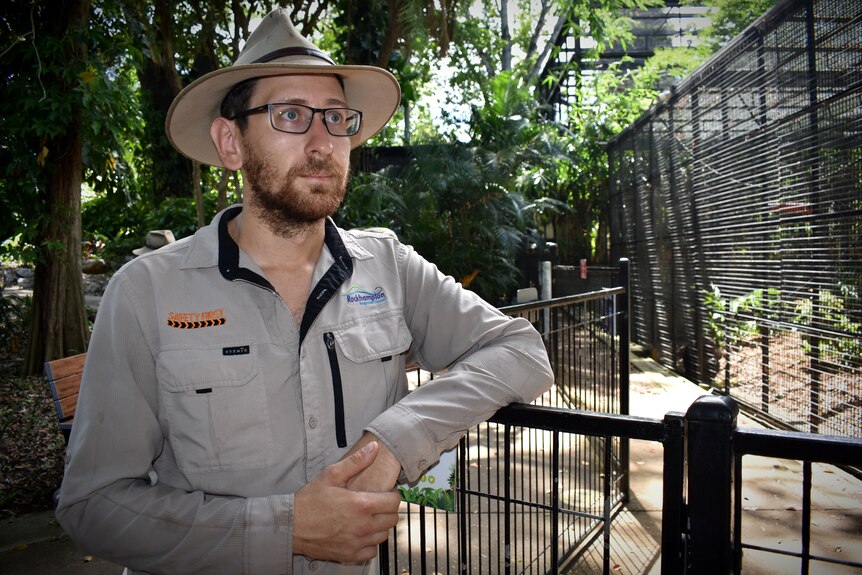 A man wearing a khaki shirt and hat standing in front of zoo enclosure