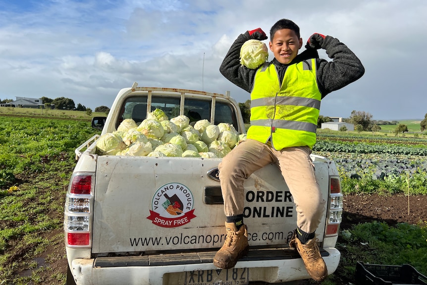 Grade 6 boy sits on edge of ute tray doing strong man pose and holding cabbage