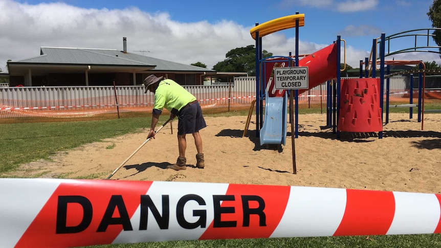 A worker rakes a playground for syringes in Esperance.