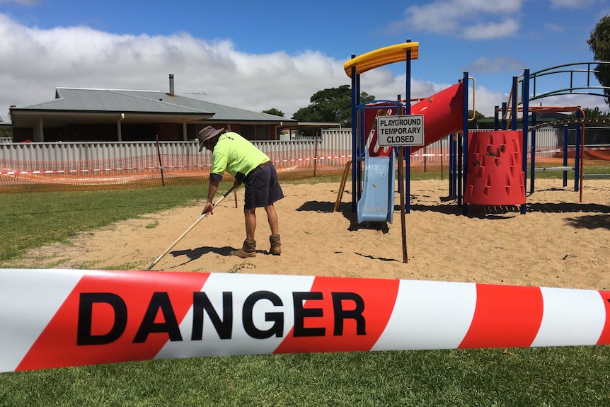 A worker rakes a playground for syringes in Esperance.
