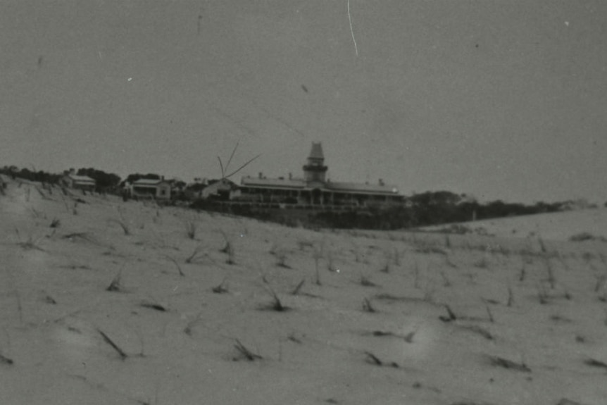 A black and white photo of a large building by the sea.