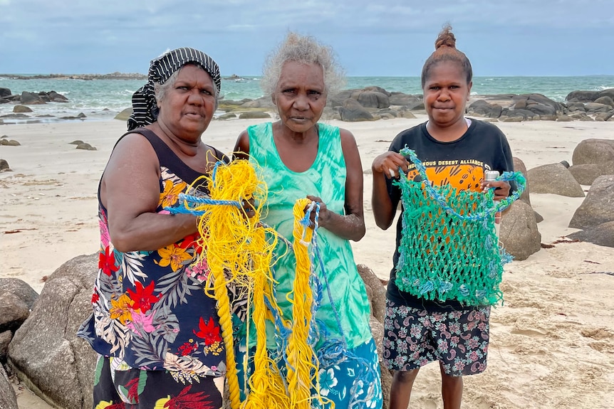 Indegenous women hold up ghost nets washe up on their beach 