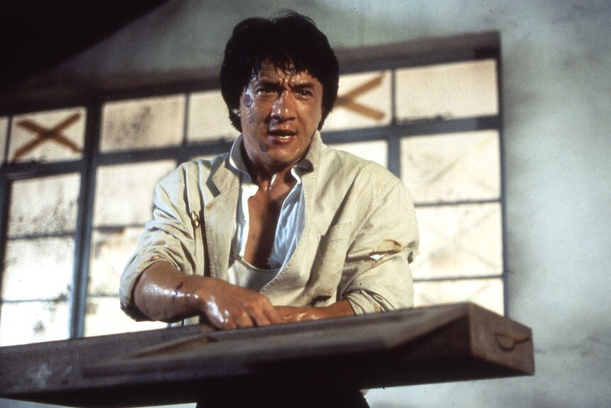 Jackie Chan holding a piece of wood, covered in sweat and cuts, in the film Police Story 2