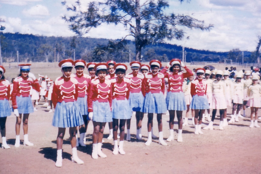 A group of Aboriginal women wearing blue skirts, red tops and hats 