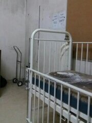 A dirty room with a hospital bed, which has a broken fan on it.