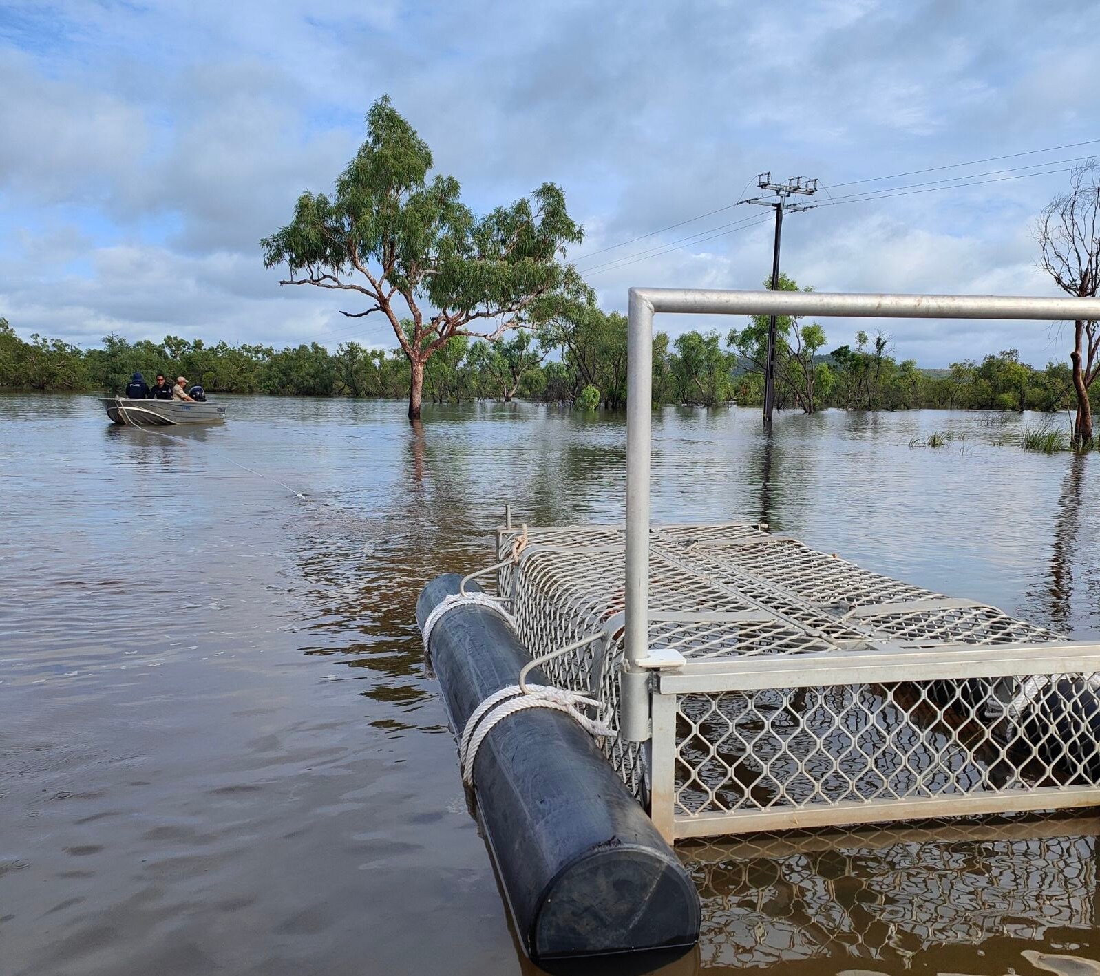 Crocodile trap sitting on the flooded Victoria Highway with small boat in the background