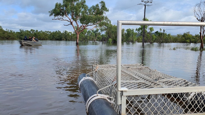 Crocodile trap sitting on the flooded Victoria Highway with small boat in the background