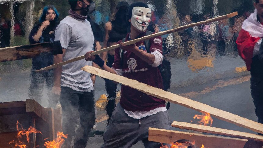 A masked protester throws a plank of wood into a burning barricade in Santiago