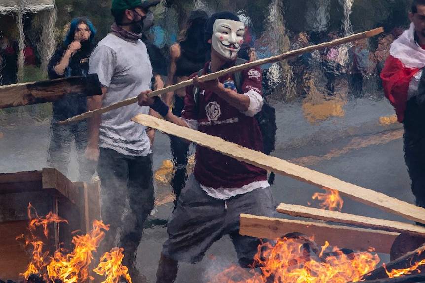 A masked protester throws a plank of wood into a burning barricade in Santiago