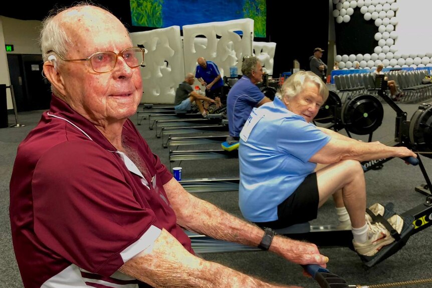 Elderly man and his wife practicing on indoor rowing machines.