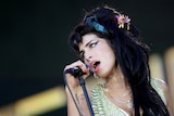 A close up of Amy who is singing into the microphone and tilting her head to the left. 