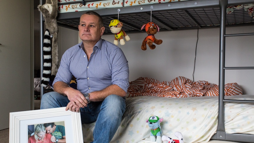 Tony Johnson in his son's bedroom holding a picture of him and his then partner and their son Victor, born at 23 weeks.