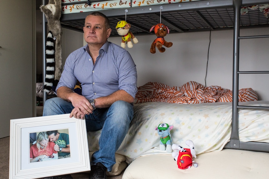 Tony Johnson in his son's bedroom holding a picture of him and his then partner and their son Victor, born at 23 weeks.