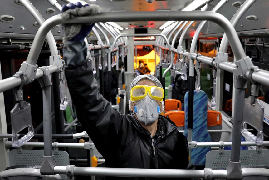 A person in wearing rubber gloves a face mask and goggles holds a railing on a bus in Tehran.
