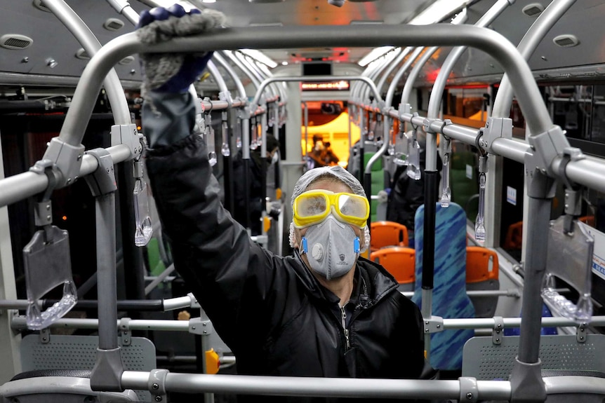 A person in wearing rubber gloves a face mask and goggles holds a railing on a bus in Tehran.