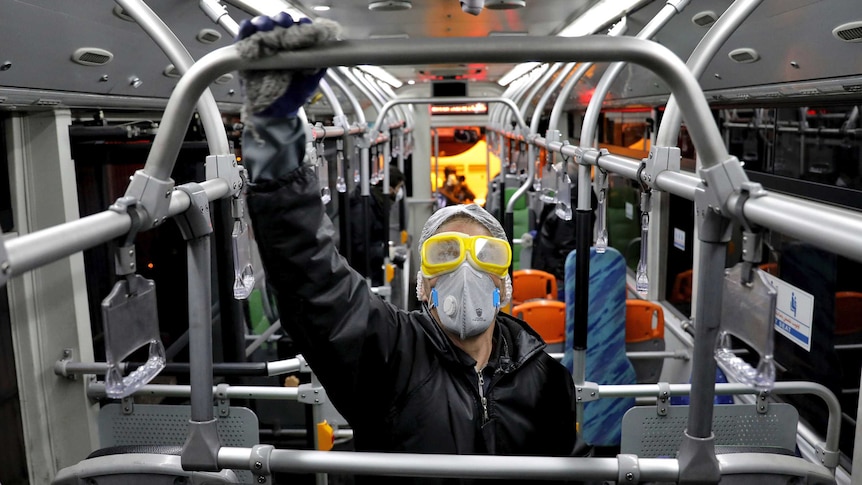 A person in wearing rubber gloves a face mask and goggles holds a railing on a bus in Tehran.