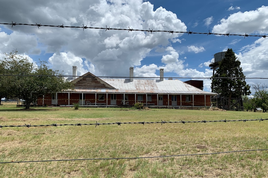 A homestead in the background with a barbed wire fence in the foreground.