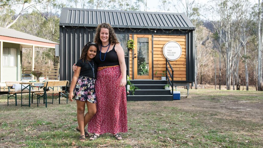 Woman and girl standing in front of tiny house in bushland