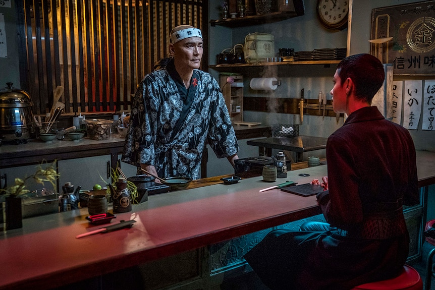 Colour still of Mark Dacascos standing behind sushi bar looking at seated Asia Kate Dillon in John Wick: Chapter 3.