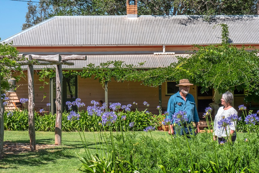 A man and woman stand in front of a classic Queenslander style house.