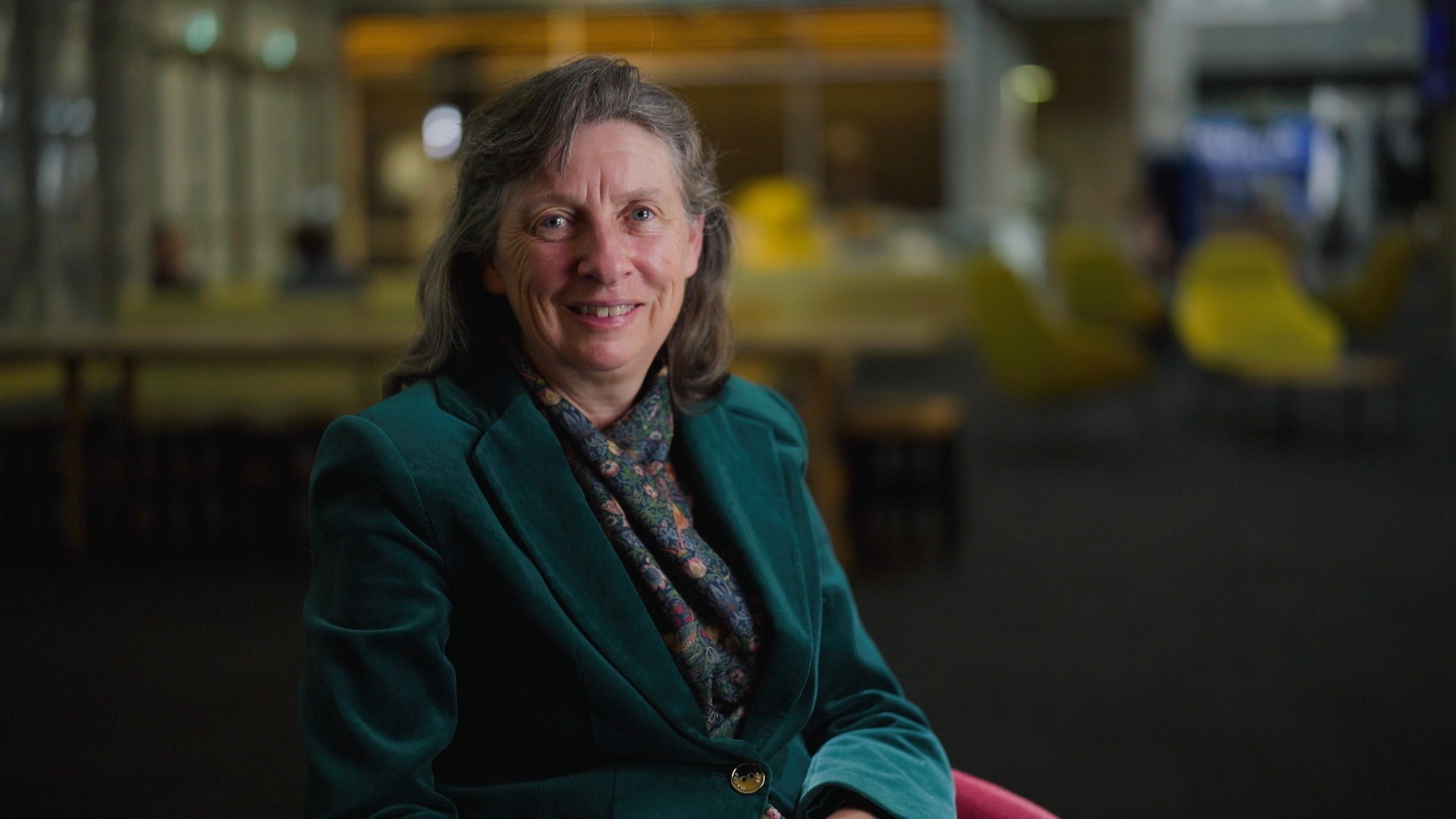 Anne Twomey com uma jaqueta verde sorrindo e o fundo desfocado.