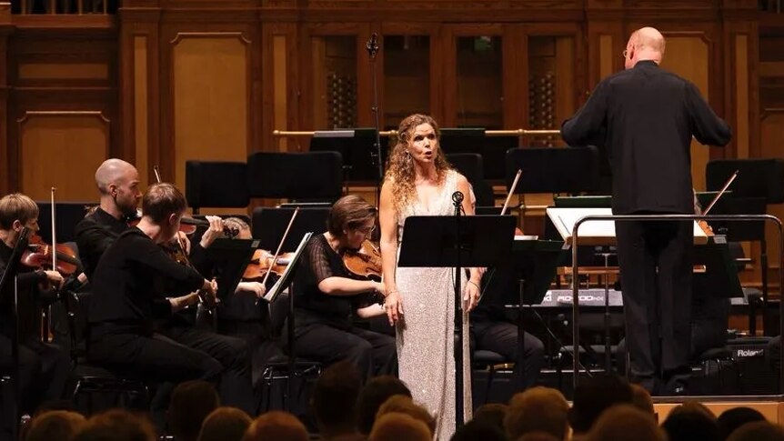 Sara Macliver sings onstage at the Adelaide Town Hall with the Adelaide Symphony Orchestra, dressed in a white gown.