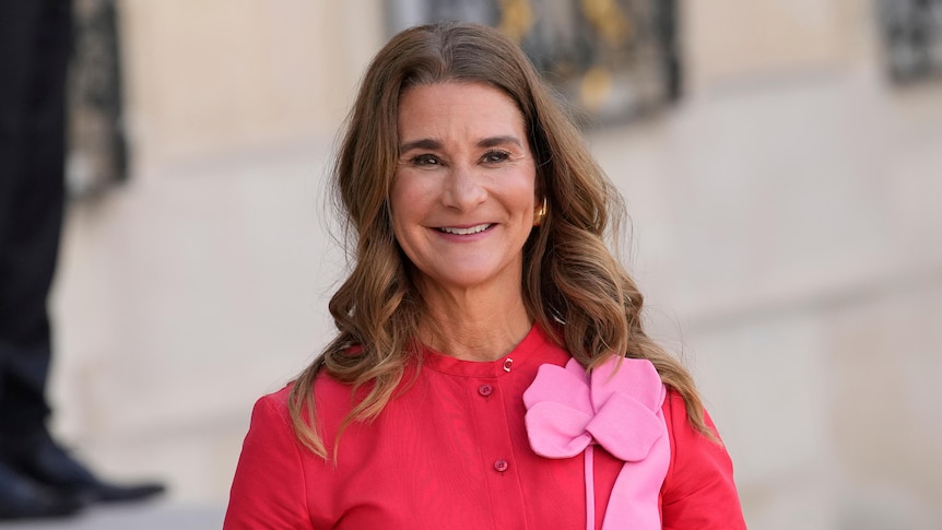 Image of Melinda French Gates, she is wearing a fuchsia top with a pink flower brooche and smiles into the camera.