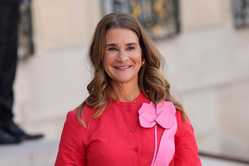 Image of Melinda French Gates, she is wearing a fuchsia top with a pink flower brooche and smiles into the camera.