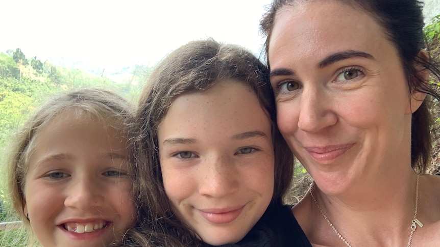 A selfie of a white woman with shoulder-length brown hair, next to two girls, who are similing.
