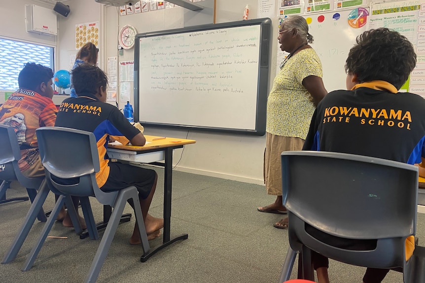 School students sit in a classroom with Aboriginal language teacher standing in front of a white board.