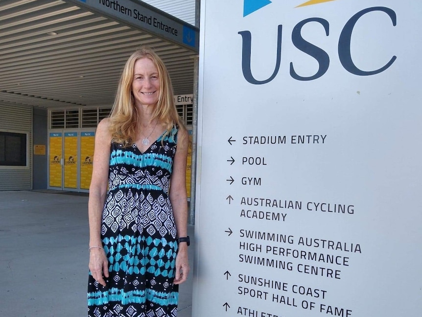 Woman standing beside sign giving directions into university facilities