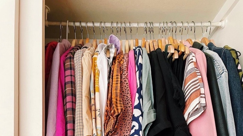 A colourful collection of clothing - dominated by pinks - on wooden coat hangers inside an in built wardrobe.