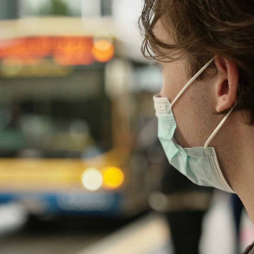 Man wearing face mask sitting at Brisbane bus stop, bus blurred in the background