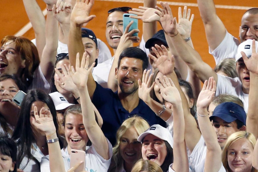 Novak Djokovic can be seen among a large number of young volunteers, waving on court