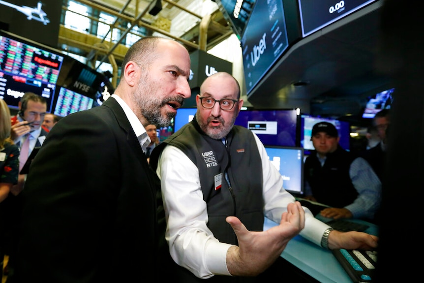 A man in a suit and a man wearing a vest with the Uber logo on it surrounded by data screens.