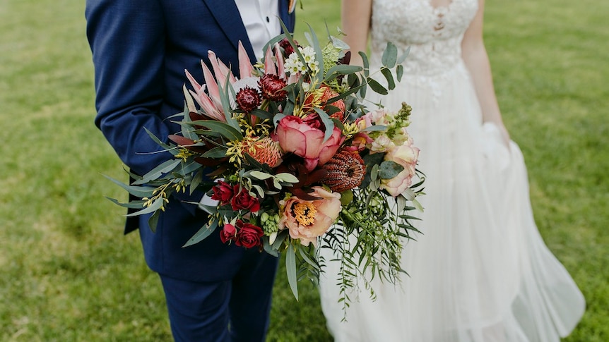 Bride and groom hold bouquet of flowers in a grassy field