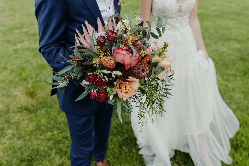 Bride and groom hold bouquet of flowers in a grassy field