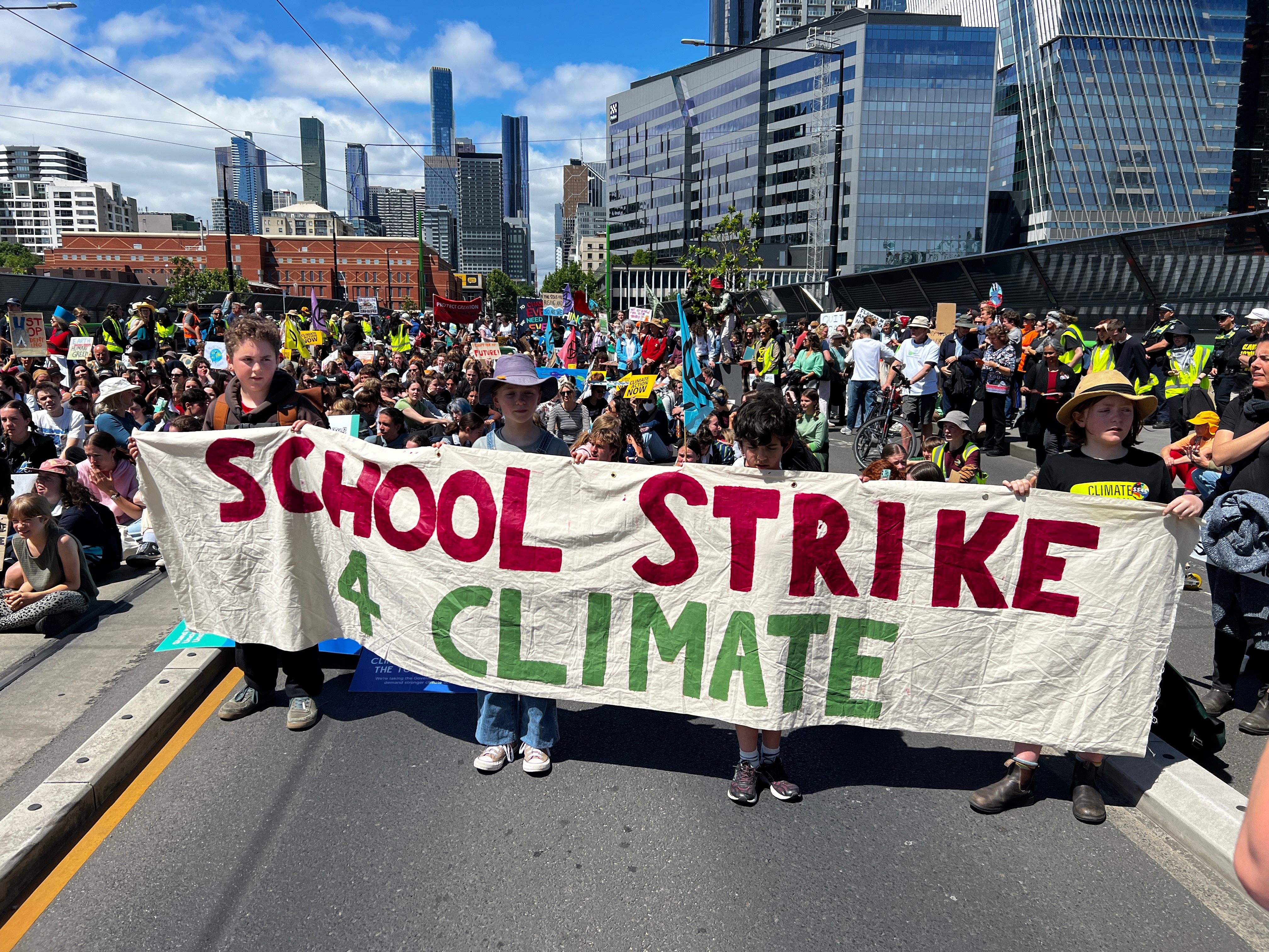 Primary school aged children holding a sign that says school strike for climate with a crowd of people behind them.