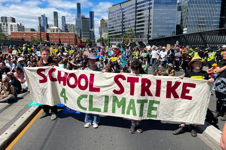 Primary school aged children holding a sign that says school strike for climate with a crowd of people behind them.