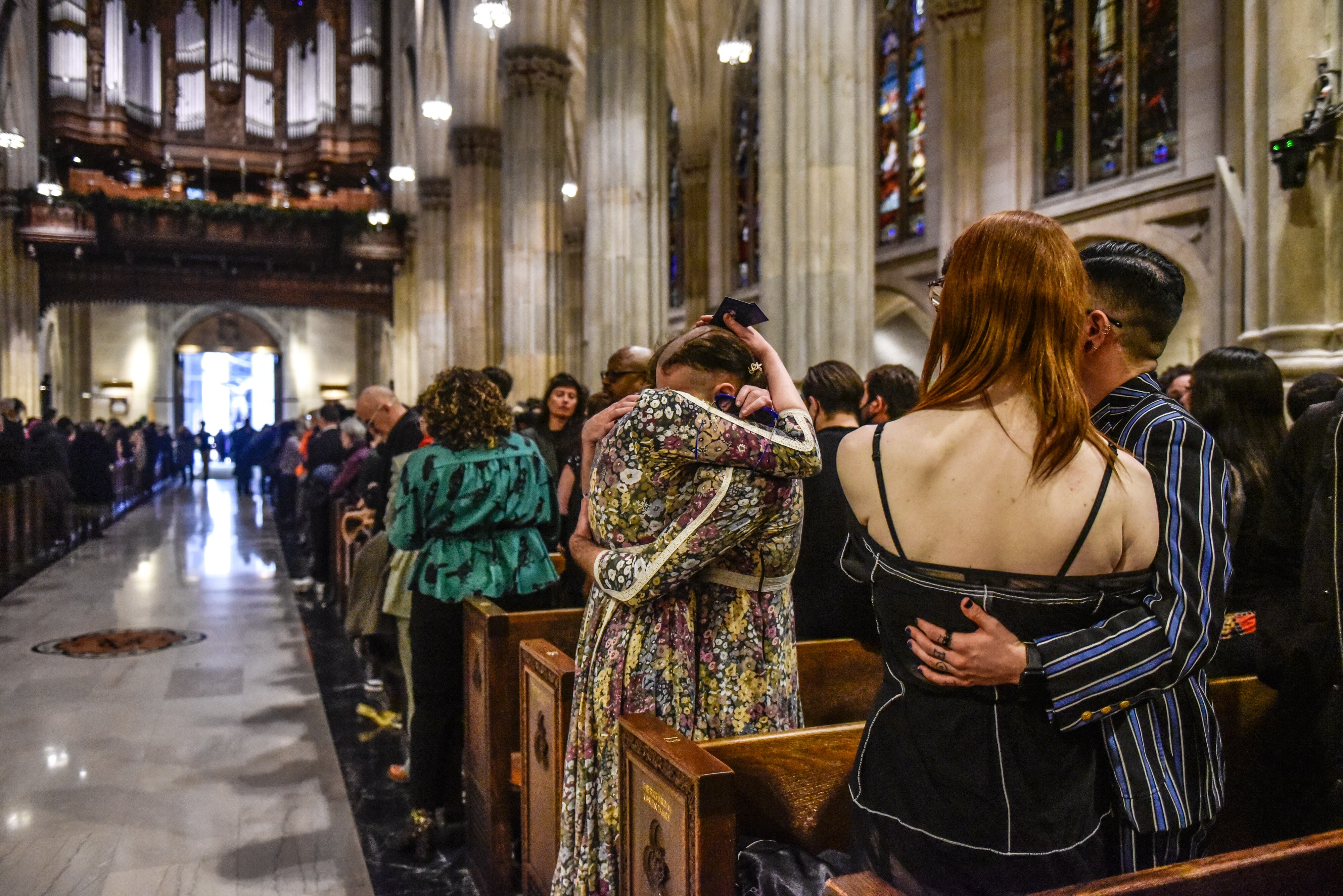 The backs of people hugging while standing in pews of a church. The church is very full.