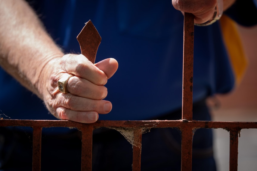 A close up shot of man's hands holding onto metal spires at a church building.