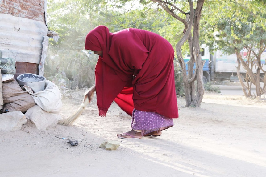 A girl in a red shawl sweeps the ground.